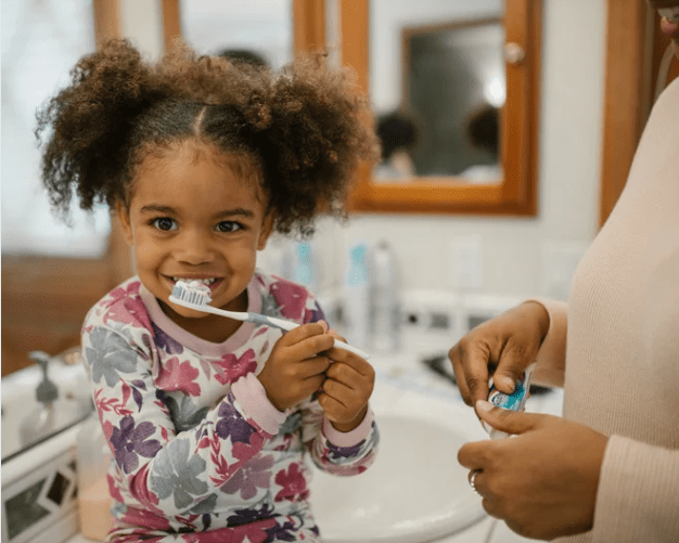 child learning to brush teeth with his mother to prevent cavities