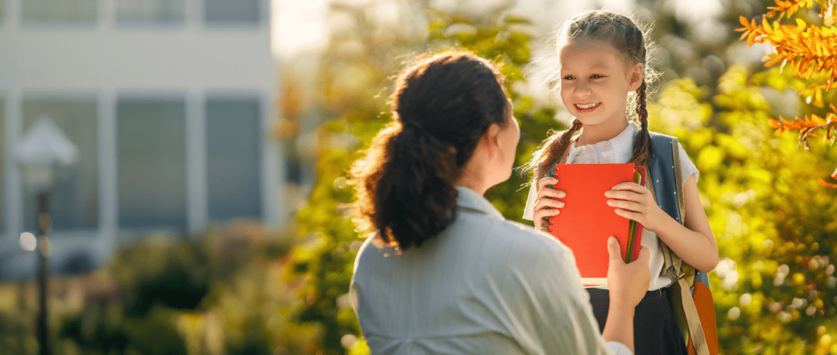petite fille heureuse qui fait sa rentrée scolaire accompagnée par sa maman à l'école
