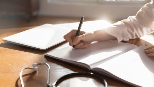 Close up woman doctor therapist writing in medical journal, sitting at table with stethoscope in office, working with documents, physician gp writing illness history, prescription in patient card